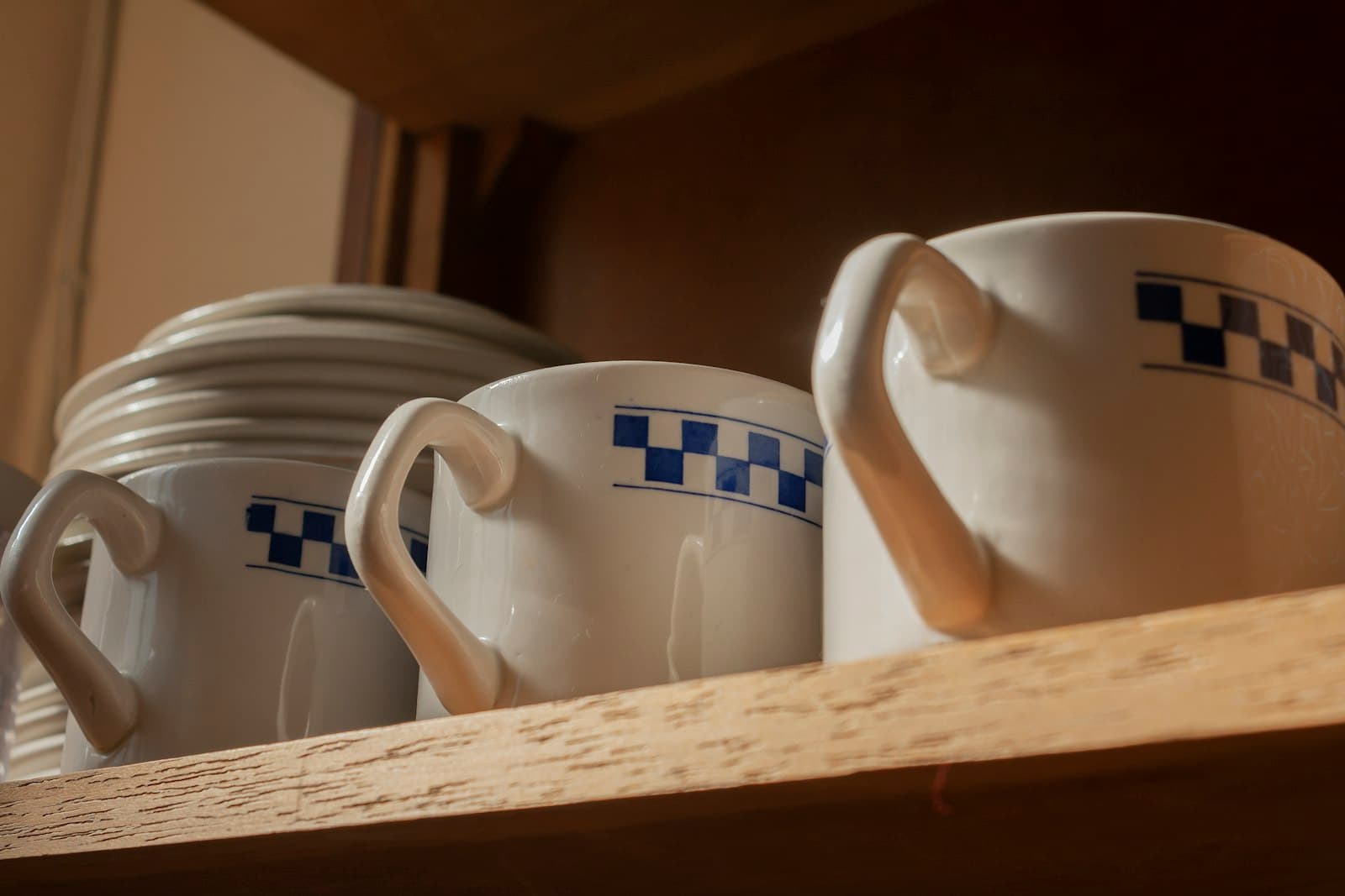 A wall shelf lined with coffee cups above a counter
