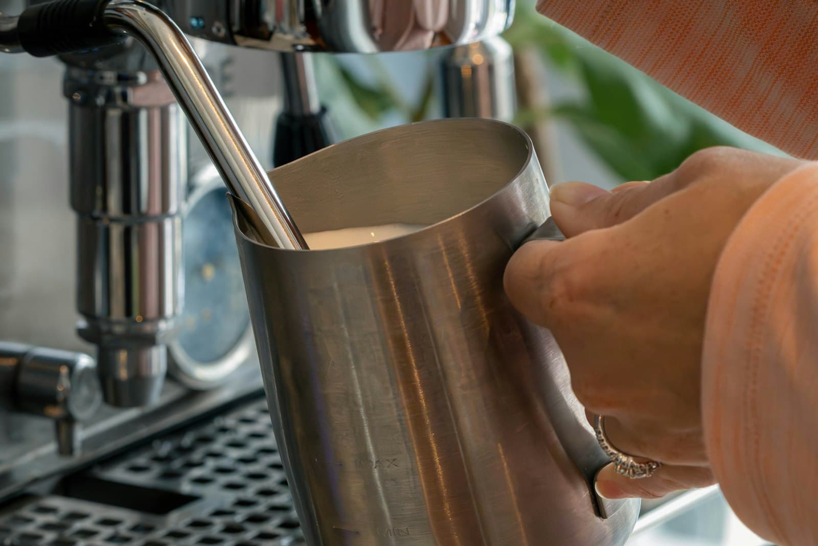 A hand steaming milk in a stainless frothing pitcher
