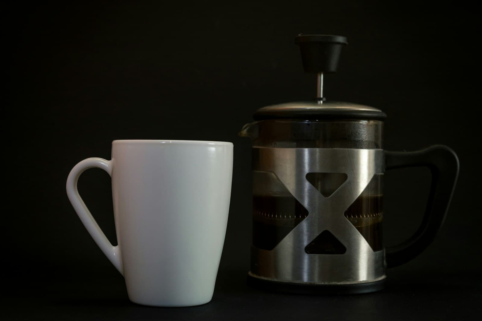 A steel French press beside a white ceramic mug