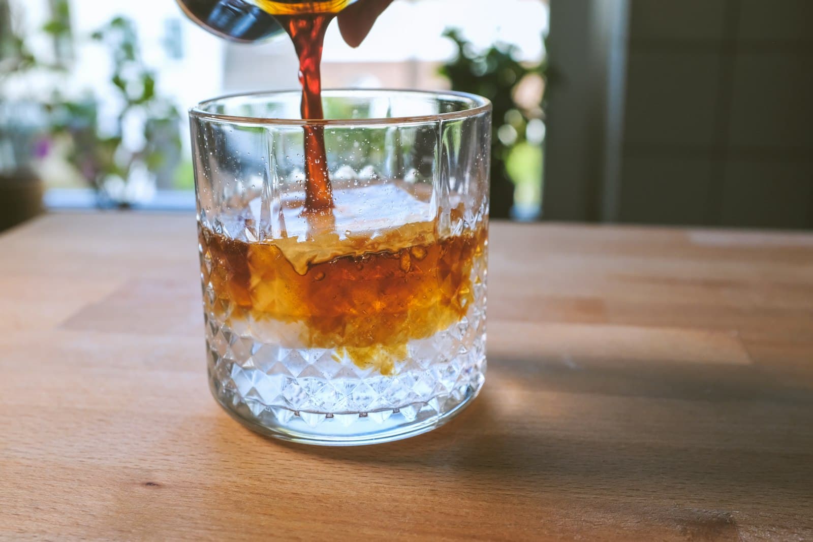 A frothy shaken coffee being poured into a glass